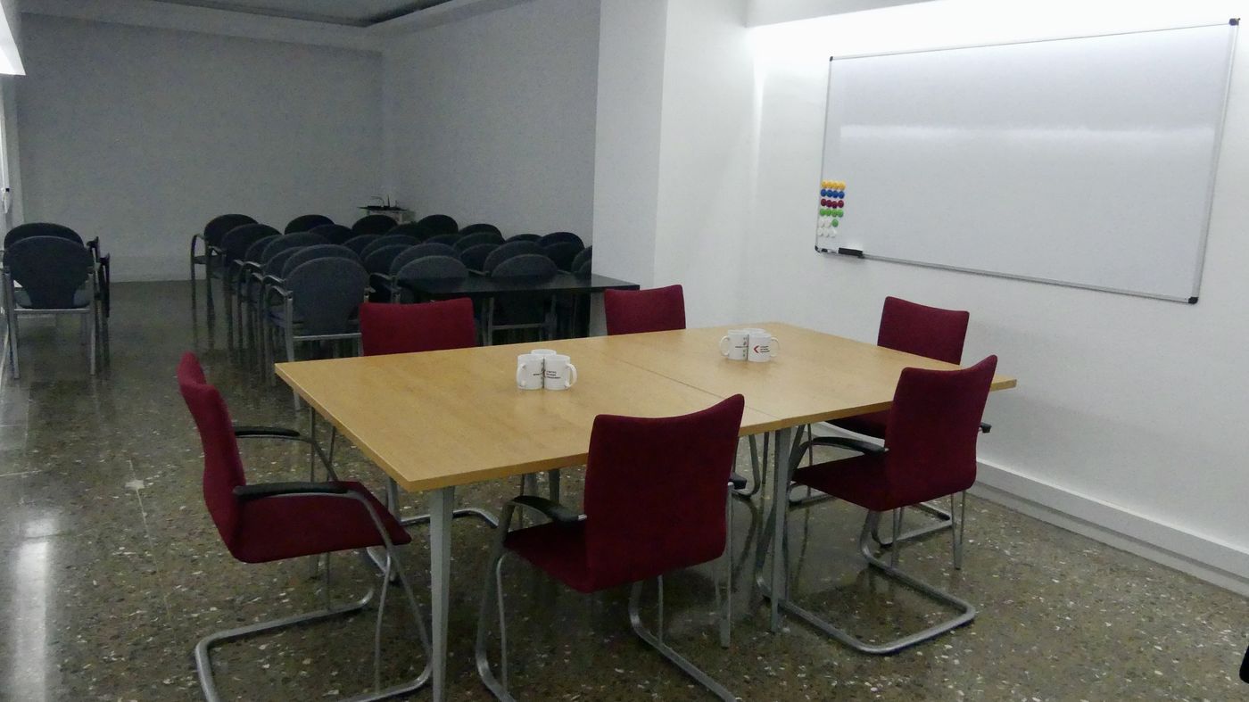 Sala de reunions gran de 40 m² amb taula de reunions, pissarra blanca i files de cadires amb tauleta al fons