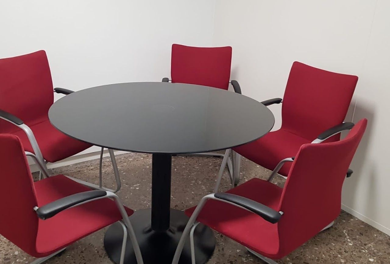 Sala de reunions petita de 15 m² amb taula rodona i cadires vermelles